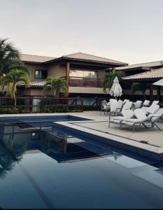 a resort with a swimming pool with white lounge chairs at Reserva itacimirim, condomínio eco itacimirim in Camacari