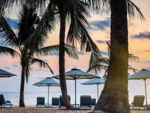 a group of chairs and umbrellas on a beach with palm trees at La Veranda Resort Phu Quoc - MGallery in Phu Quoc