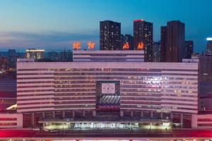 a large building with a clock on it in front of a city at E-Cheng Hotel Shenyang North Railway Station in Shenyang