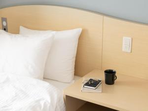 a bed with a book and a cup on a table at Brackets Hotel Osaka Hommachi in Osaka