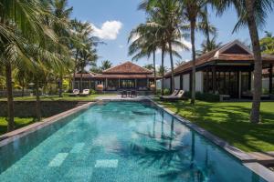 a swimming pool in front of a house with palm trees at Four Seasons The Nam Hai, Hoi An, Vietnam in Hoi An