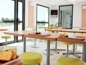 a cafeteria with tables and chairs with bread on them at ibis budget Niort - La Crèche in La Creche