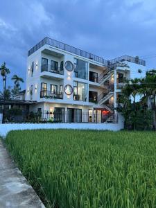a white building with a grass field in front of it at Betel Hoi An Homestay in Cam Thanh