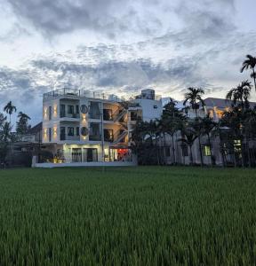 a large white building with a field in front of it at Betel Hoi An Homestay in Cam Thanh