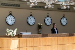 a woman standing behind a counter with clocks on the wall at Saint Sofia Golf Club, Hotel and SPA in Robertowo
