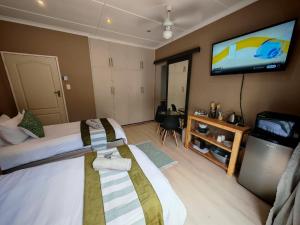 ein Hotelzimmer mit zwei Betten und einem Flachbildfernseher in der Unterkunft The Lion's Den in George