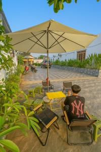 un hombre sentado en una silla bajo una sombrilla en Avina Hotel Đắk Nông, 
