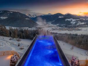 a swimming pool in the snow with mountains in the background at Alpin Panorama Hotel Hubertus in Valdaora