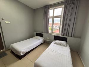 Dos camas en una habitación pequeña con ventana. en Ho Hotel Batu Berendam, en Malacca