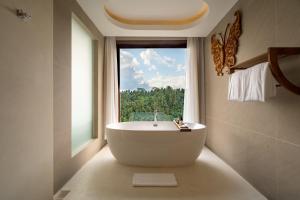 a bath tub in a bathroom with a window at Sanggraloka Ubud in Ubud