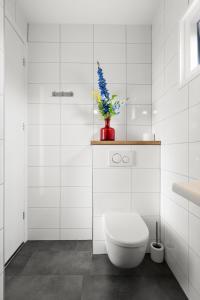 a white bathroom with a toilet and a vase with flowers at NEW! Vakantiehuis Grijpskerke met airco en houtkachel - 2 personen in Grijpskerke