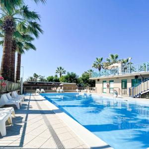 a large swimming pool with palm trees and a building at Happy Camp mobile homes in Duca Amedeo Camping Village in Martinsicuro