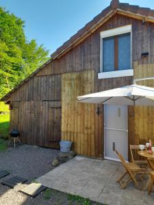 a wooden barn with a table and an umbrella at Gîte de charme avec jacuzzi étang babyfoot et rivière in Belonchamp