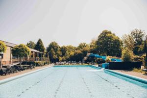 an empty swimming pool with chairs and trees at Luxe 12-persoons Groepsvilla – Gelijkvloers met Tuin & Loungeset in Apeldoorn