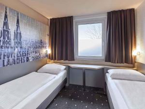 a small room with two beds and a window at B&B Hotel Köln-West in Cologne