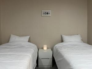 two beds with white sheets and a candle on a night stand at Stay Ducksan in Suwon