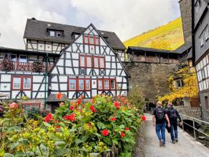 two people walking in front of a house with red flowers at Bacchus Holiday Homes in Bacharach