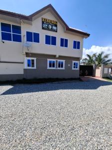 a white building with blue windows on a gravel driveway at King'sol Guesthouse in Kasoa