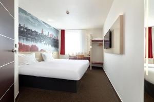 ein Hotelzimmer mit einem weißen Bett und einem Fernseher in der Unterkunft B&B Hotel Warszawa-Okęcie in Warschau