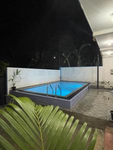 a pool at night with a palm tree in the foreground at FEEL Beach Apartments in Kalutara