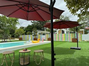 two tables and two umbrellas in front of a pool at บ้านสวนแสงหล้า วิลล่า รีสอร์ท in Ban Nong Khayat
