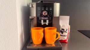 een koffiezetapparaat met twee oranje kopjes op een plank bij Appart 2 Chambres Charley super emplacement et parking in Calvi