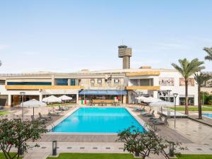 a pool in front of a building with chairs and umbrellas at Novotel Cairo Airport in Cairo