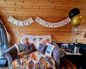 a couch with a happy birthday sign and balloons at Forester's Retreat Glamping - Dinas View - Dogs over the age of 2 with vaccination accepted RALI CEREDIGION EVENT 4TH-6TH SEP 2026 in Aberystwyth