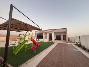 un patio trasero con un parque infantil con un tobogán en شاليه خيال, en Sanāw