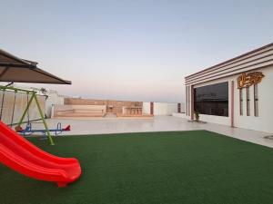 Un patio trasero con un tobogán rojo y un parque infantil en شاليه خيال, en Sanāw