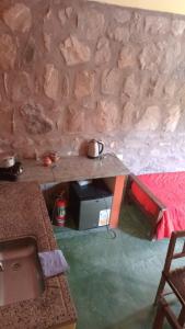 ein Raum mit einer Steinmauer mit einem Tisch mit einer Mikrowelle in der Unterkunft Mirá el Cardón in Tilcara