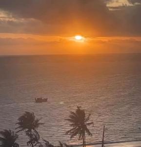 a boat in the ocean at sunset with palm trees at Flat Vista-Mar in Cabedelo