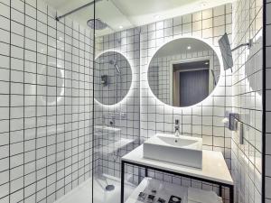 a white tiled bathroom with a sink and a mirror at Mercure Paris la Défense Grande Arche in Nanterre