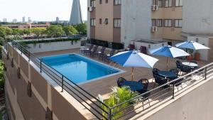 a balcony with a swimming pool with umbrellas and chairs at Hotel Metrópole Maringá in Maringá