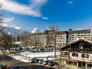 a building with cars parked in a parking lot with mountains at Mercure Hotel Garmisch Partenkirchen in Garmisch-Partenkirchen