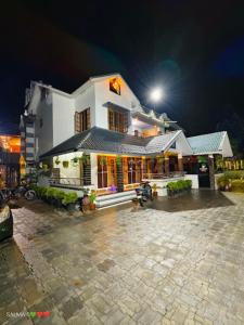 una gran casa blanca por la noche con un estacionamiento en Mountain Vibes Wayanad Pool Villa and Spa, en Wayanad