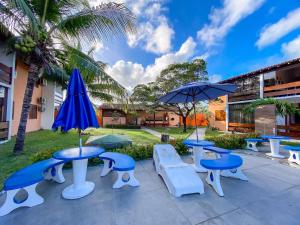 a group of tables and chairs with umbrellas at Flat com 1 quarto com ar split, sala e cozinha completa, No condomínio Portal do Atlântico a 100m praia de Taperapuã (Barraca do Gaúcho) , portaria 24hrs, piscina. in Coroa Vermelha