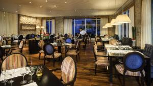 グアルジャにあるHotel Jequitimar Guaruja Resort & Spa by Accor - Ex Sofitelのテーブルと椅子が備わるレストランで、背景に人がいる