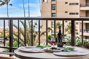 una mesa con una botella de vino y copas en el balcón en Sugar Beach 304, en Kihei