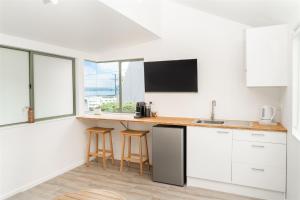 a kitchen with white cabinets and a counter with stools at BEACH Baby Cottage! in Ngunguru