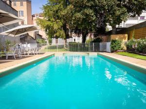 a large blue swimming pool with chairs and an umbrella at ibis Styles Macon Centre in Mâcon