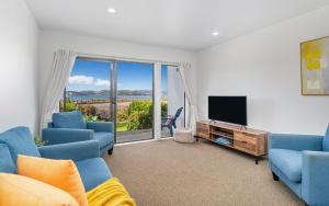 a living room with two blue chairs and a television at Sea Views at 7 - Beachside Apartment in Whitianga