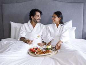 a man and woman sitting in bed with a tray of food at Pullman Sydney Hyde Park in Sydney