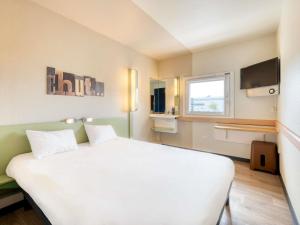 a bedroom with a large white bed and a window at ibis budget Versailles - Trappes in Trappes