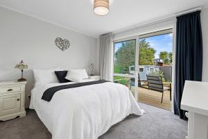 a white bedroom with a bed and a balcony at Hannahs Bay Haven - Rotorua Holiday Home in Rotokawa