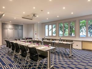 Una sala de conferencias con mesas, sillas y ventanas. en Mercure Paris Saint Cloud Hippodrome, en Saint-Cloud