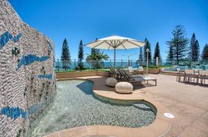 a patio with an umbrella and a table and bench at 5-Star Beachfront Retreat with Theatre & Pool in Mooloolaba