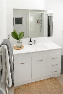 a white bathroom with a sink and a mirror at BEACH Baby Cottage! in Ngunguru