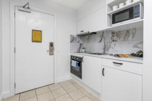 a white kitchen with white cabinets and a microwave at Sky Tower View with Rooftop Pool! in Auckland