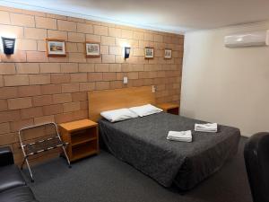 a room with a bed and a chair and a brick wall at The Lodge Village & Motel, Moranbah in Moranbah